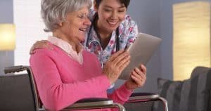 a senior elderly lady and a caregiver sharing a fun moment together watching reading from an ipad