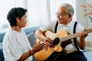 senior elderly couple happily playing guitar and singing together on sofa at home